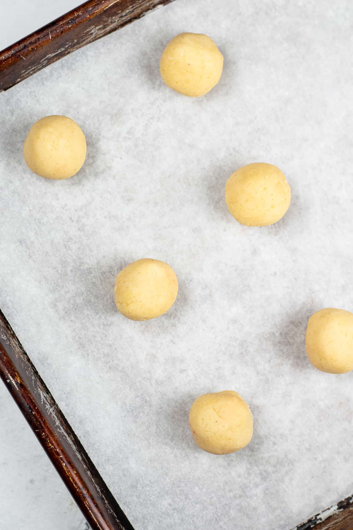 Cookie dough balls spaced out on a baking sheet lined with parchment paper from above.