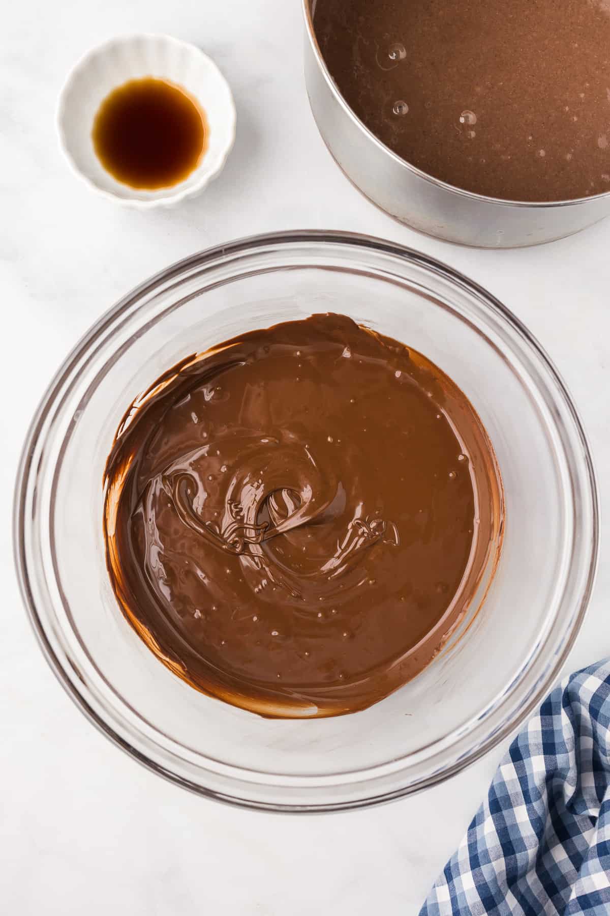 Melted chocolate in a large bowl from overhead with a small bowl of vanilla and a pot with chocolate inside nearby.