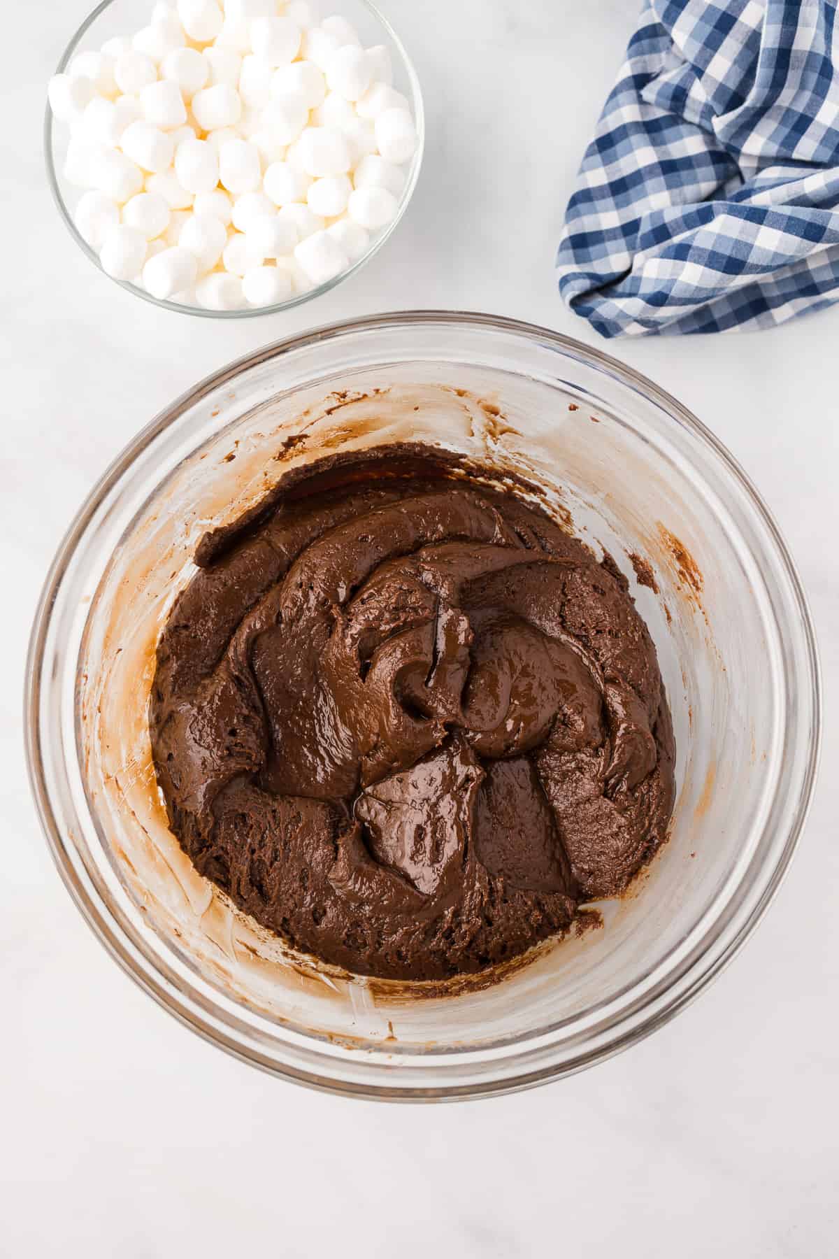 Hot chocolate fudge mixture thickened in a large bowl from overhead with a bowl of mini marshmallows nearby.
