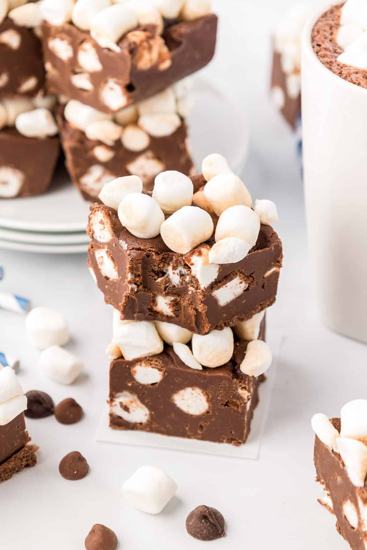 Two pieces of chocolate fudge full of marshmallows stacked with the top piece missing a bite and more on a platter in the background.