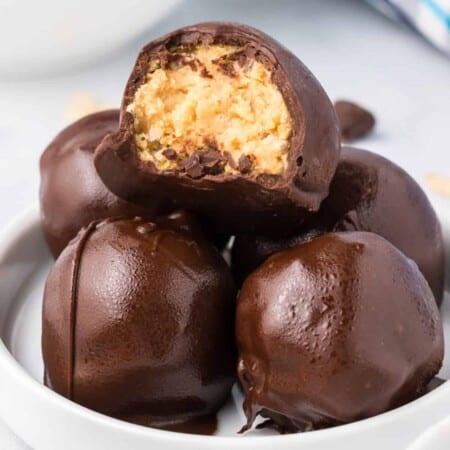 Stack of peanut butter rice krispie balls coated in chocolate with the top chocolate missing a bite close up from the side on a plate.