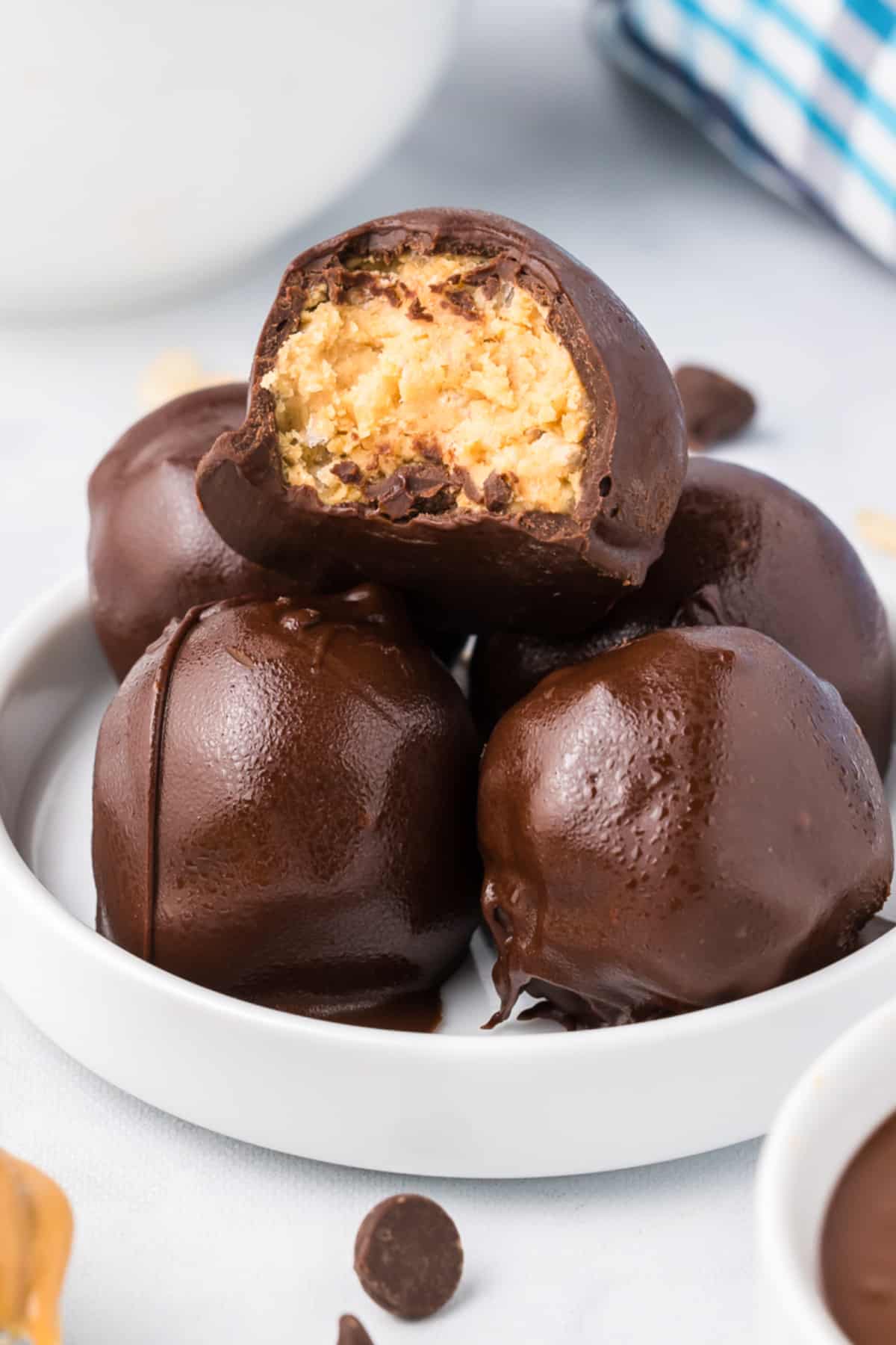Peanut butter balls with rice krispies stacked on a small plate on a counter from the side with the top truffle missing a bite to see the inside.