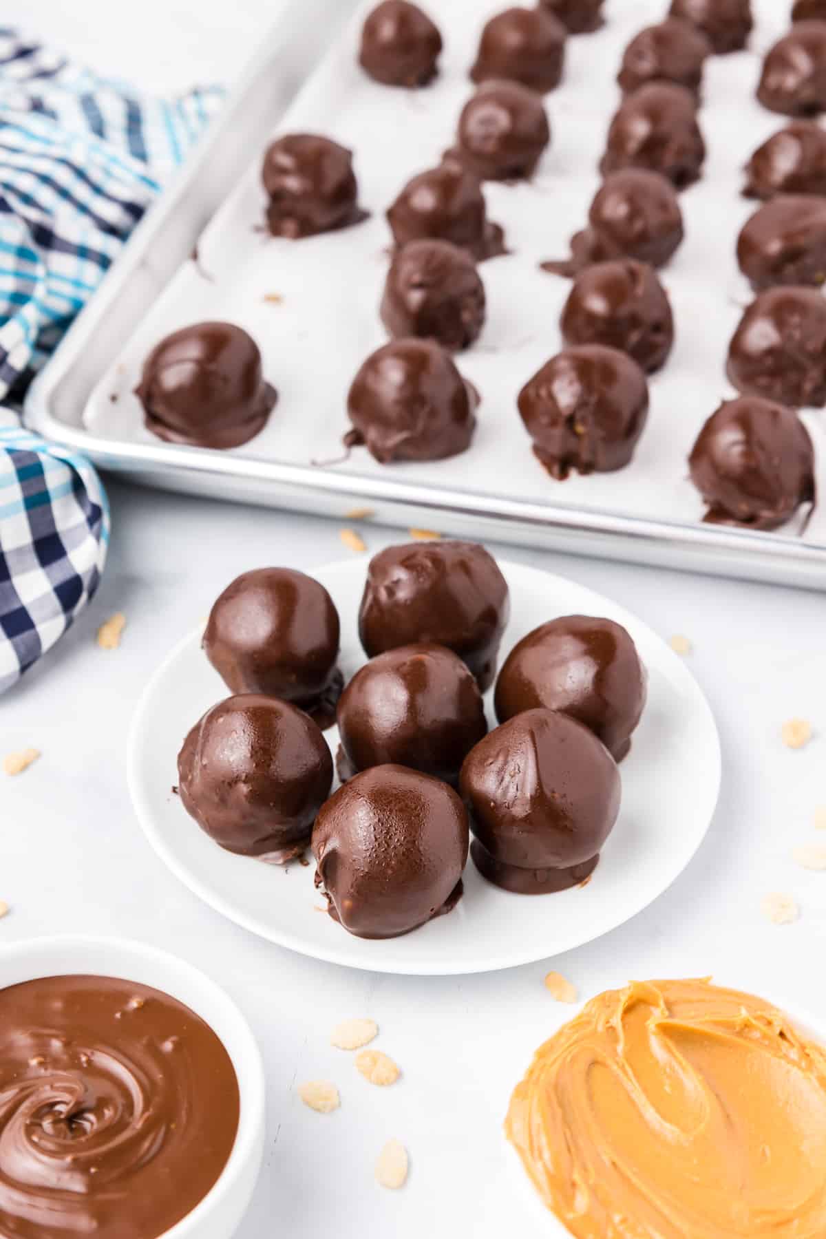 Peanut butter rice krispie balls being stacked on a plate on a counter with more treats lined up on a baking sheet lines with parchment paper in the background.