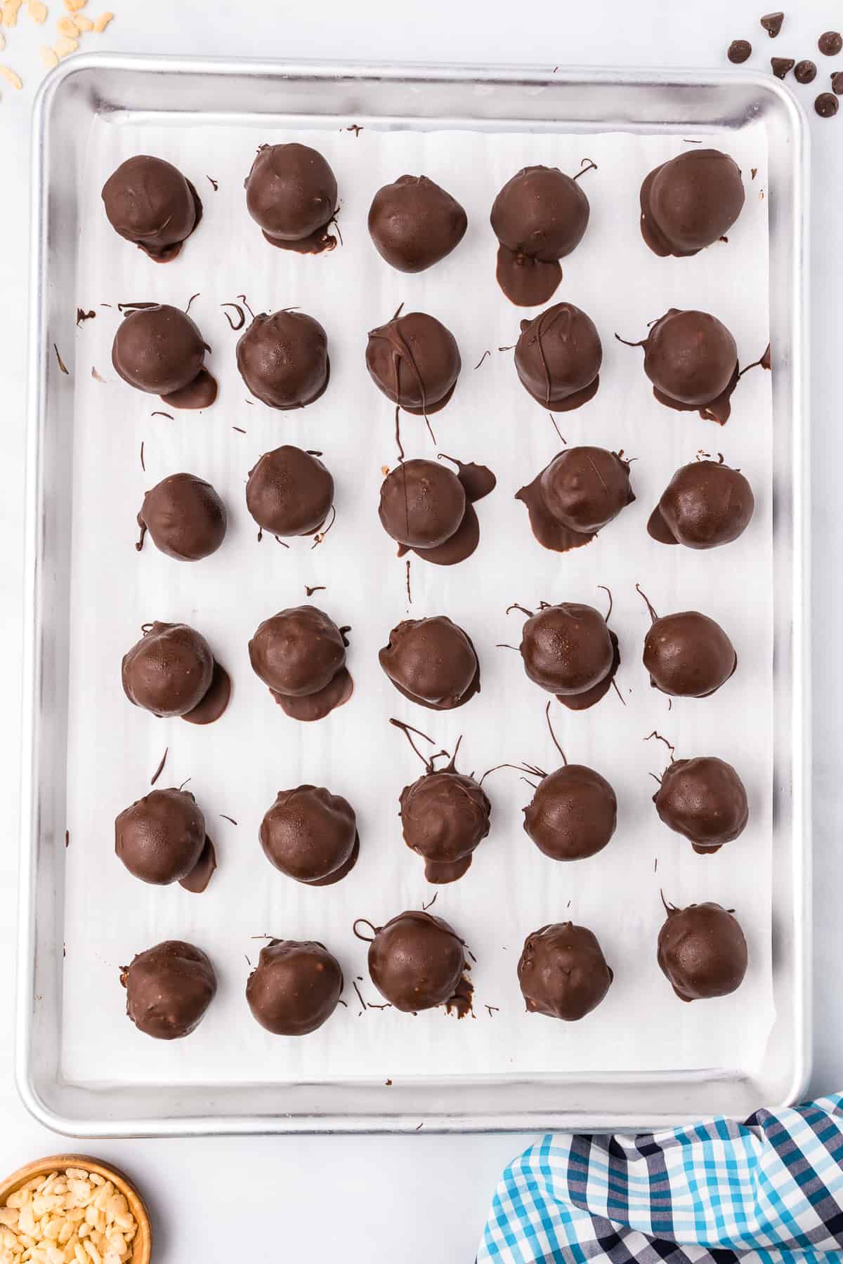 Peanut butter rice krispie balls dipped in chocolate spaced on pan lined with parchment paper from overhead on a counter.