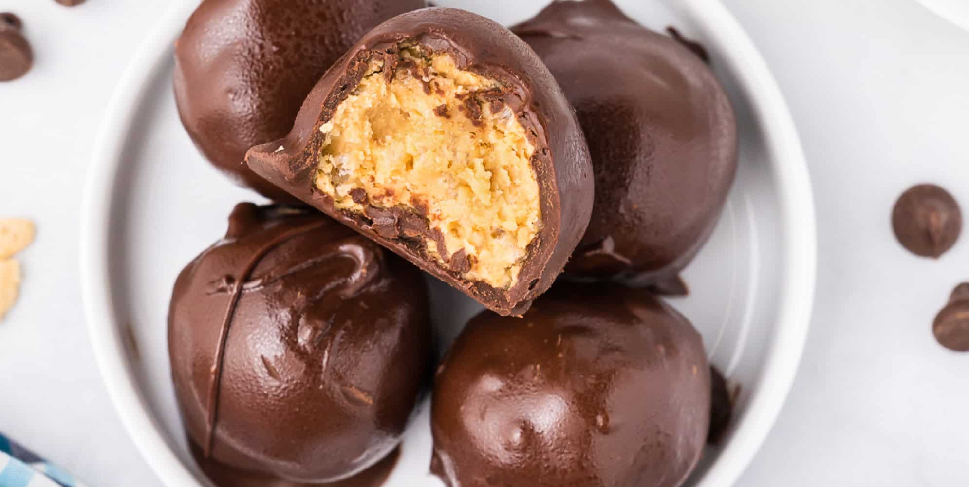 Overhead view on a counter of a small plate full of peanut butter balls with the top piece missing a bite to show inside the chocolate shell.