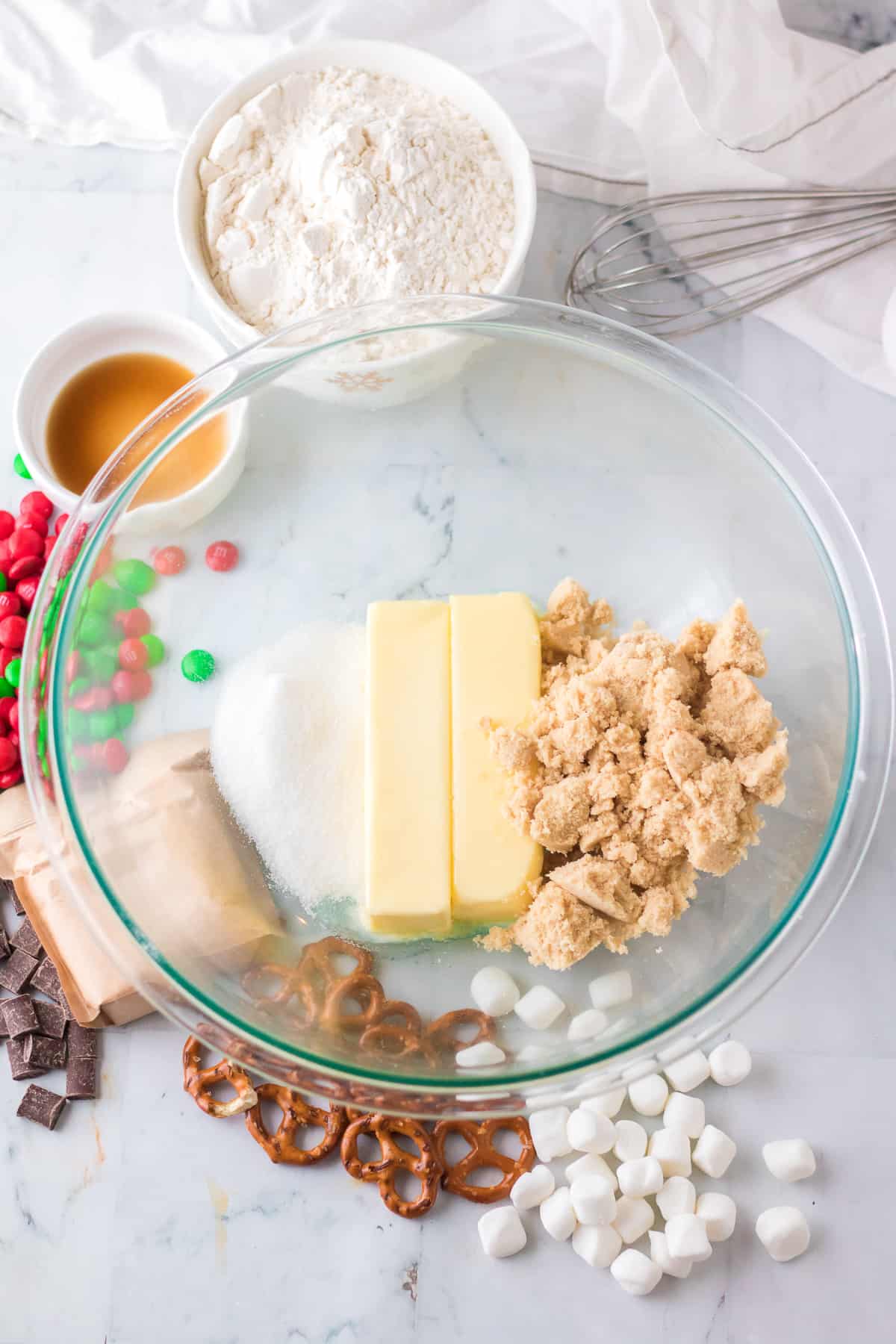 Butter, brown sugar and white sugar in a mixing bowl on a counter from overhead with other cookie ingredients on the counter nearby.