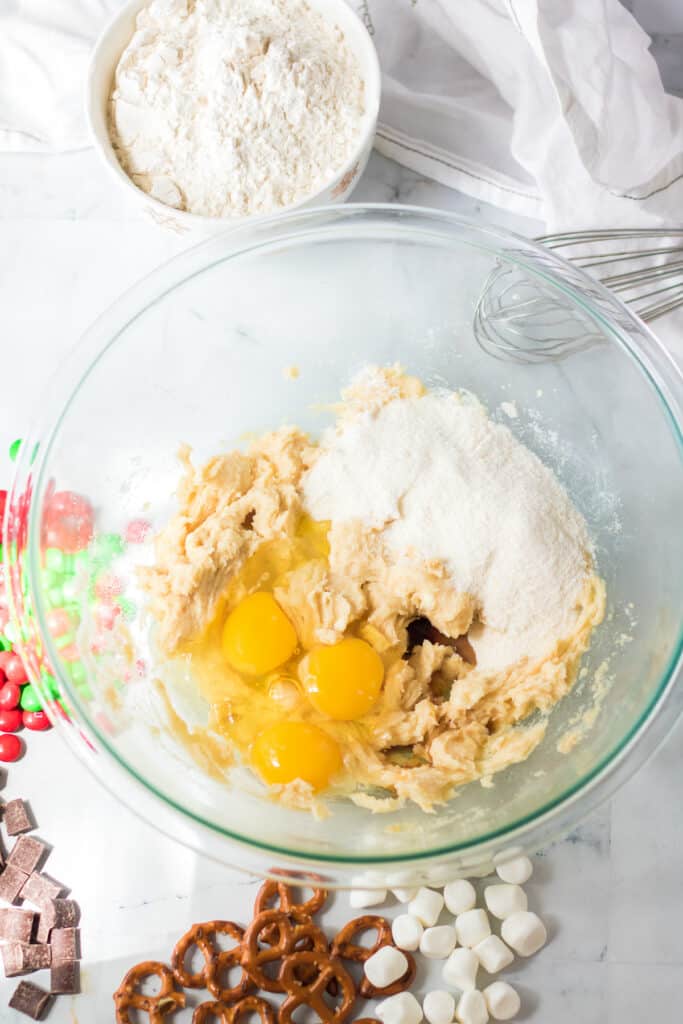 Eggs, wet ingredients and pudding mix being mixed into creamed butter sugar mixture in a large bowl on a counter from overhead with more ingredients on the counter nearby.