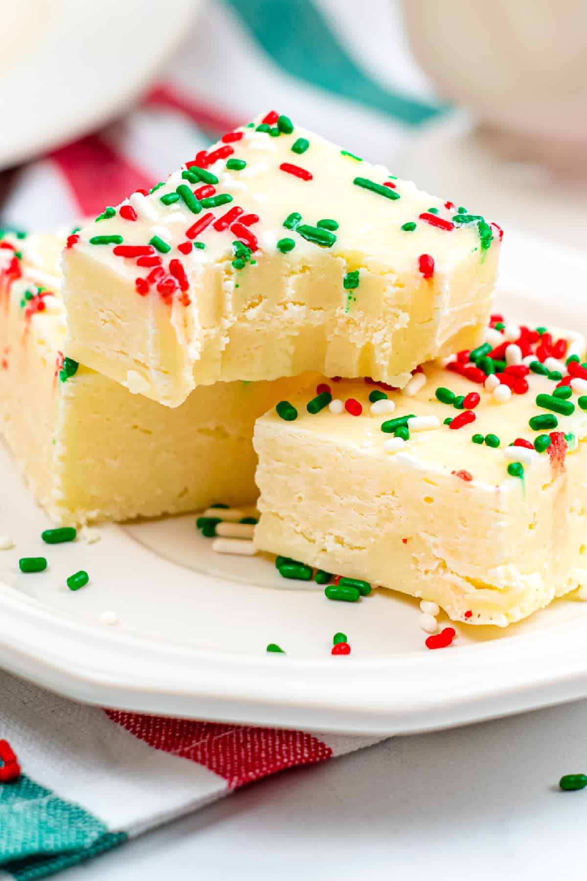 Sugar cookie fudge piled on a plate from the side with the top piece missing a bite.