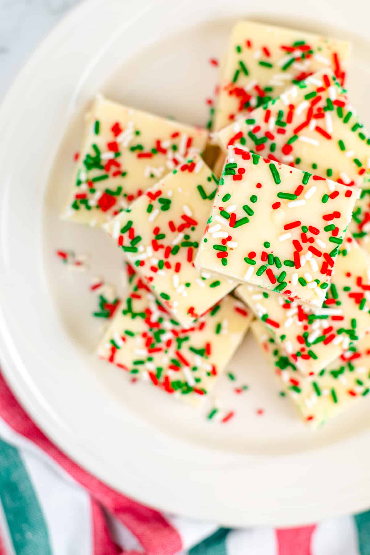 Sugar cookie fudge piled on a plate with red and green sprinkles from overhead on a counter.