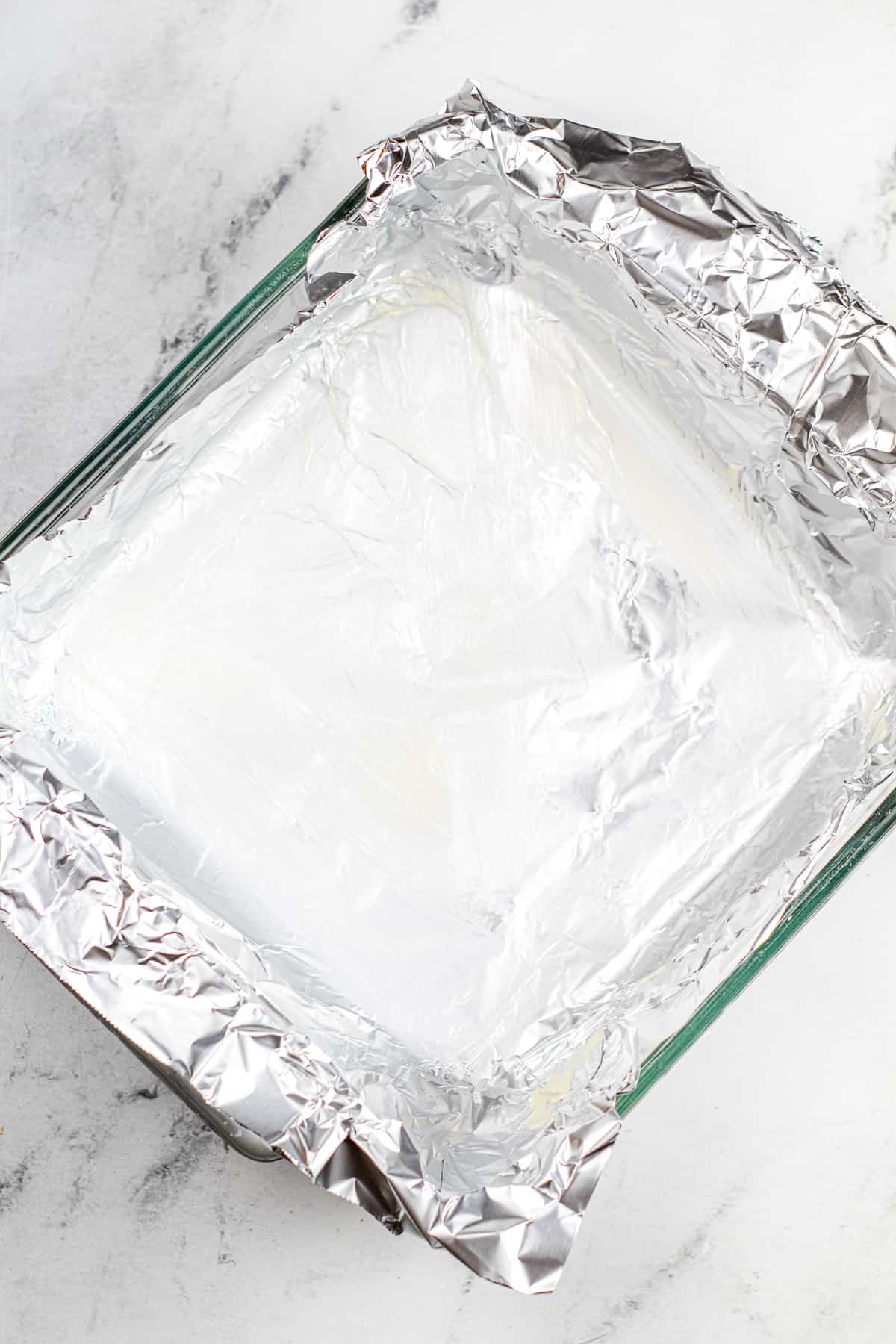 A square pan from overhead tilted at an angle and lined with aluminum foil coated in butter.