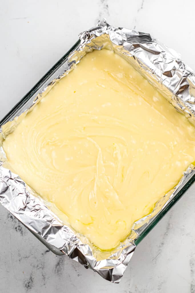 Sugar cookie fudge in a aluminum foil lined pan on a counter from overhead tilted at an angle.
