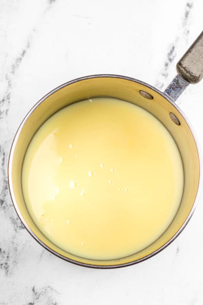 Sweetened condensed milk and butter mixed together in a sauce in a saucepan from overhead on a counter for sugar cookie fudge.