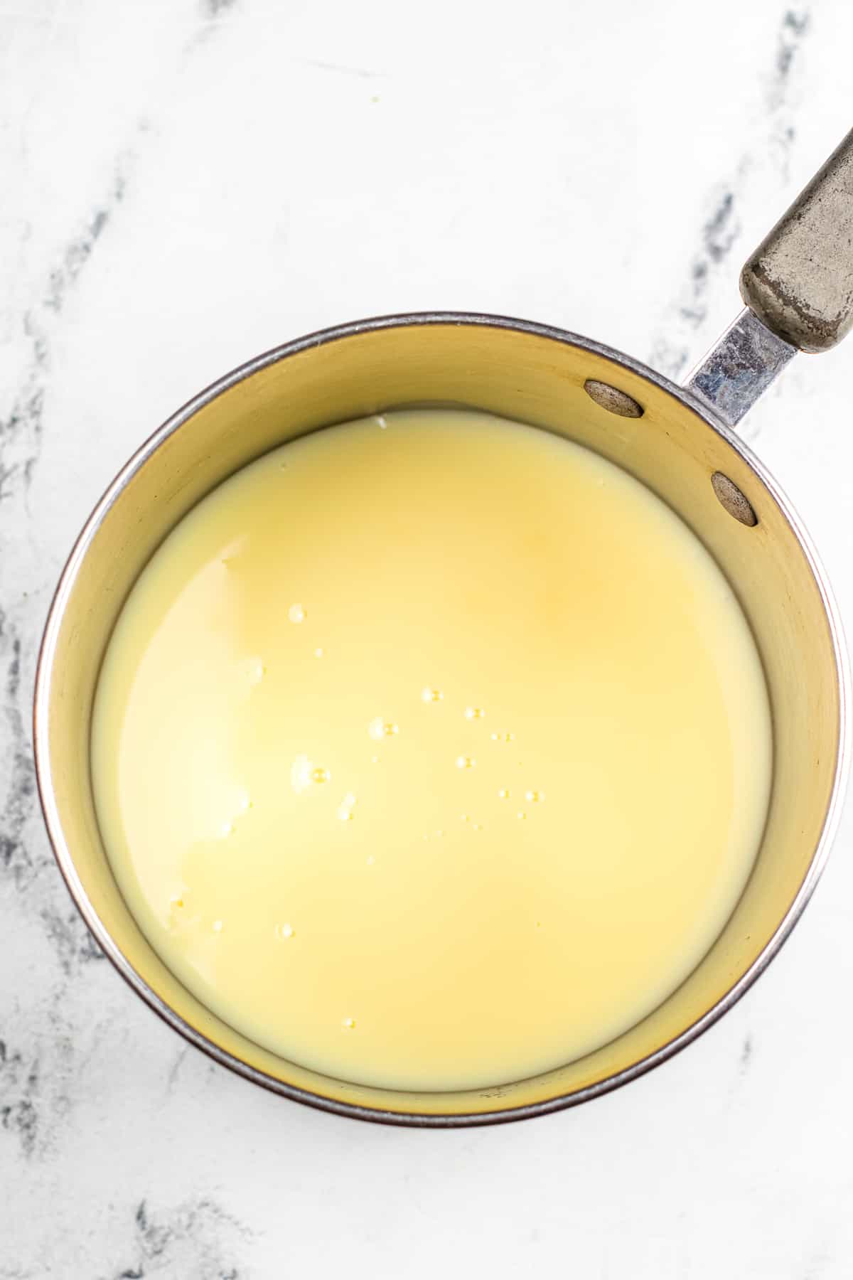 Sweetened condensed milk and butter mixed together in a sauce in a saucepan from overhead on a counter.