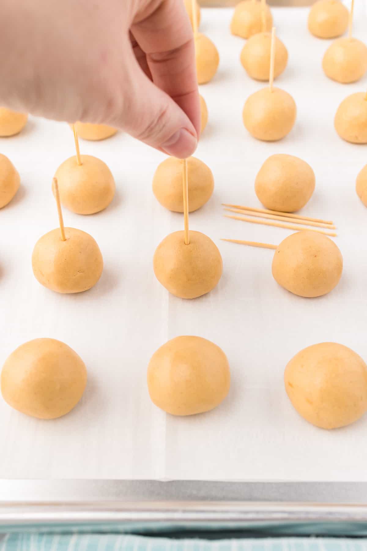 Toothpicks being placed in each peanut butter dough ball on a sheet pan from the side.