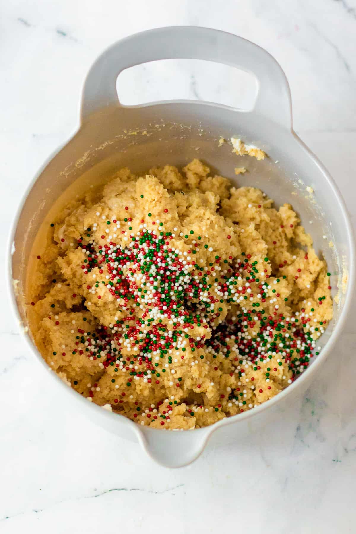 Golden oreo cream cheese dough in a mixing bowl with christmas nonpareil sprinkles being mixed into the dough.