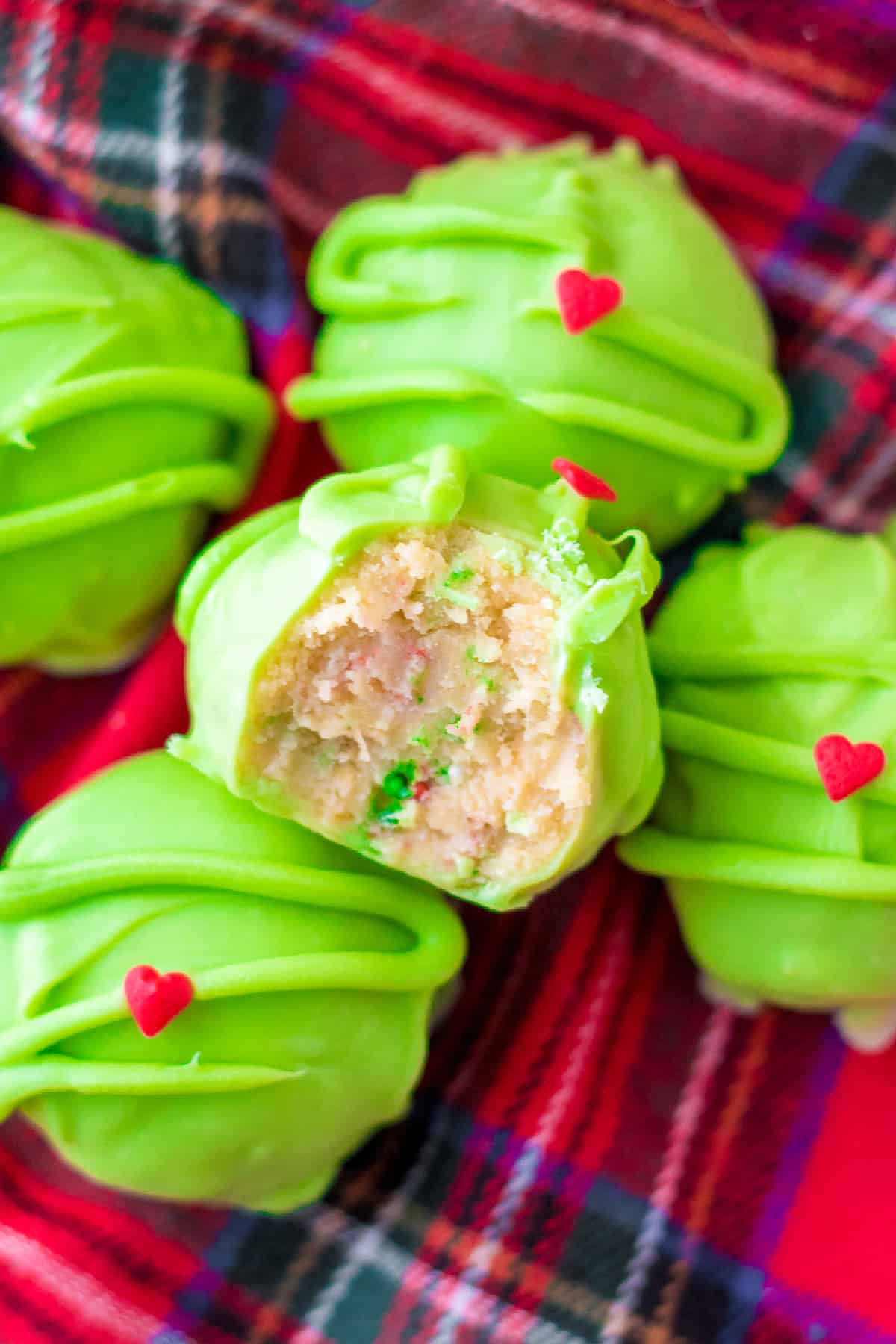 Grinch inspired green golden Oreo truffles stacked from overhead on a christmas napkin with the top truffle missing a bite.