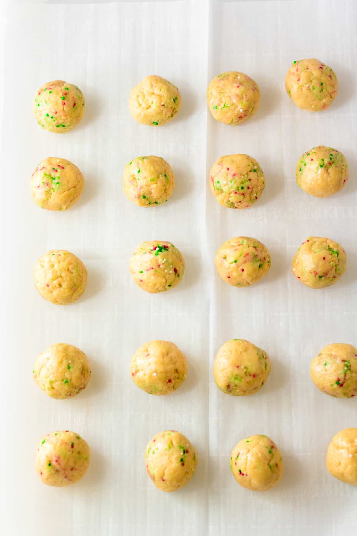 Golden oreo ball truffles with red and green sprinkles mixed into the dough rolled on a piece of parchment paper.