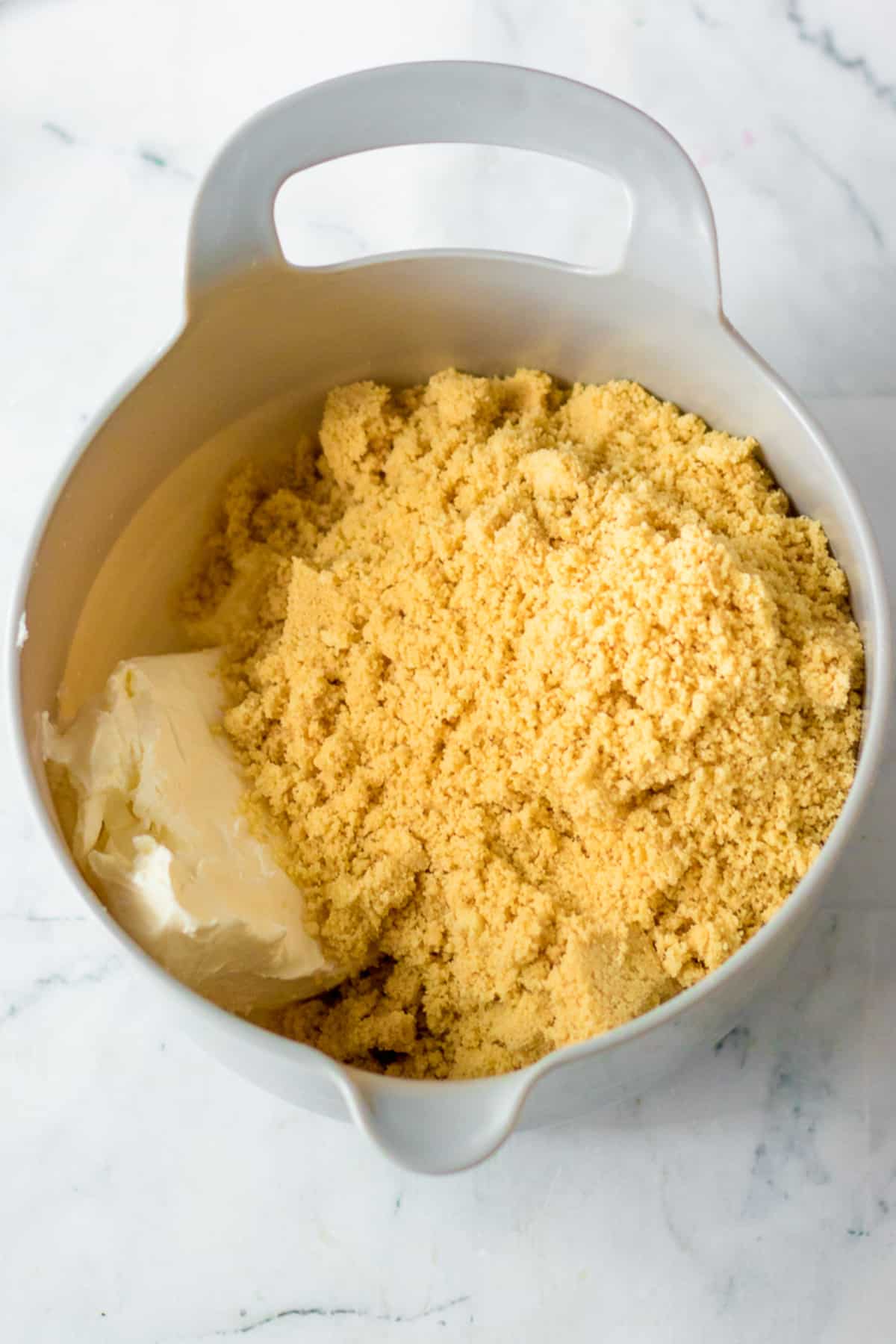 Mixing cream cheese and golden oreo cookie crumbs together in a mixing bowl from overhead on a counter.