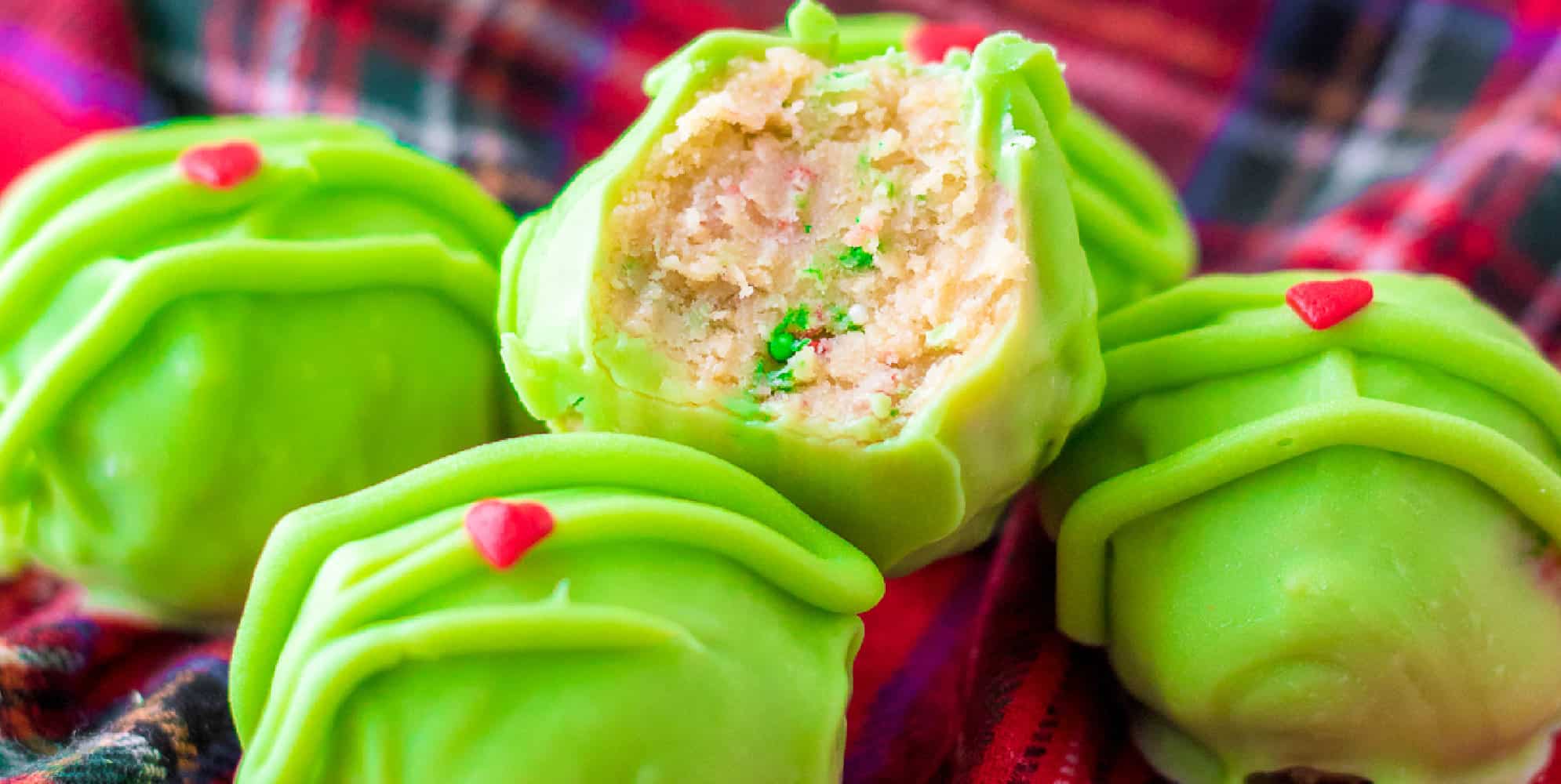 Wide view of golden oreo truffles coated in grinch green chocolate topped with a heart sprinkle with the top truffle missing a bite.