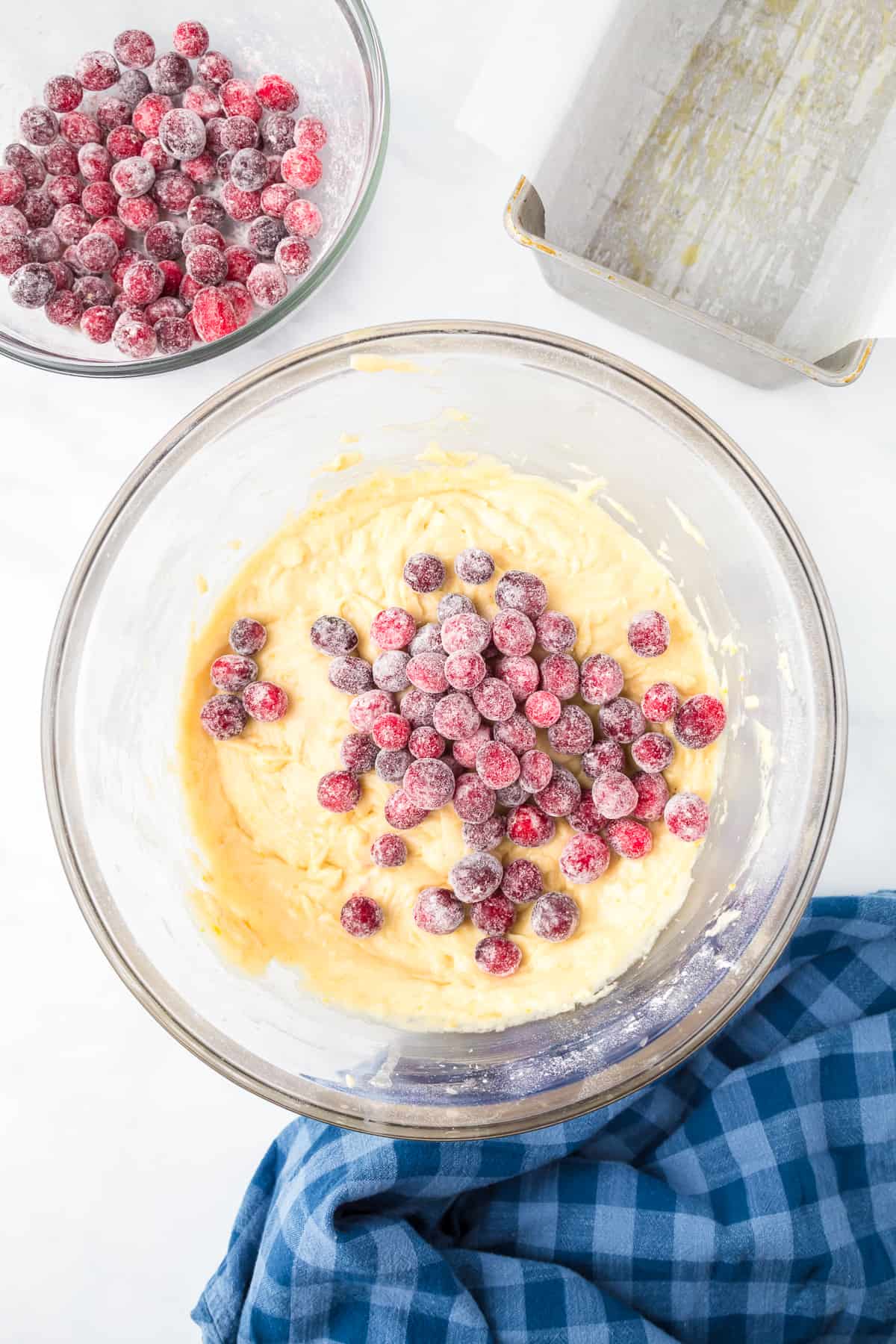 Cranberries being folded into an orange cake batter in a bowl from above on a counter.