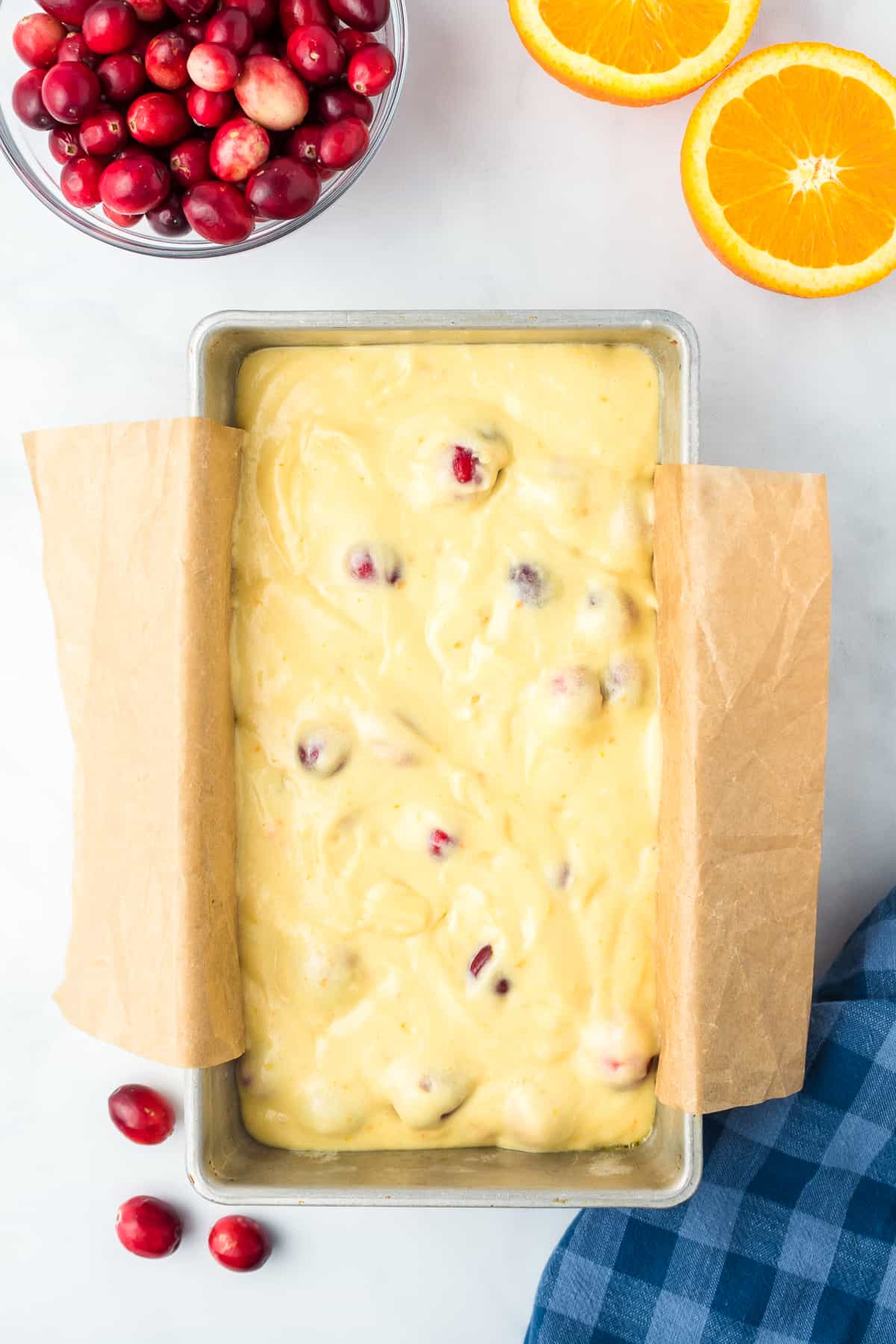 Cranberry orange batter in a loaf pan lined with parchment paper from above on a counter.