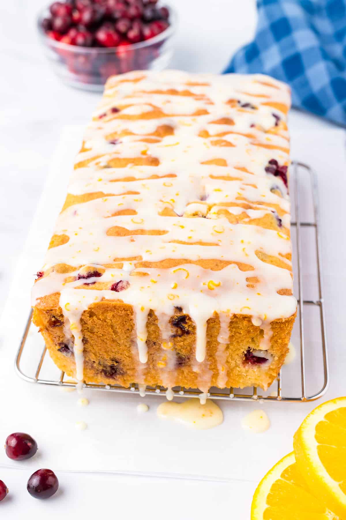 Cranberry orange bread on a wire rack from the end with a glaze drizzled across the entire loaf on a counter.