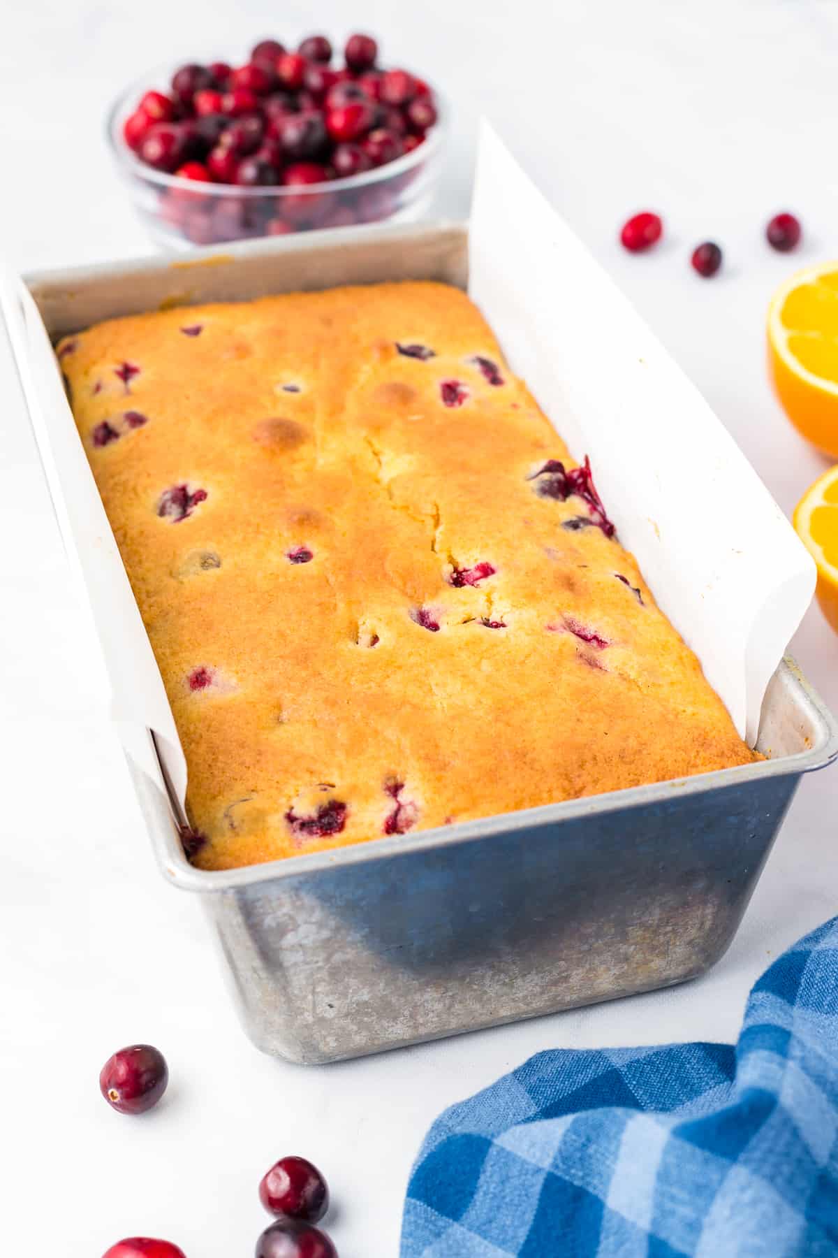 Baked cranberry orange bread in loaf pan from the side on a counter.