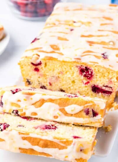 Sliced cranberry orange bread topped with glaze at an angle on a platter to see the entire sliced loaf.