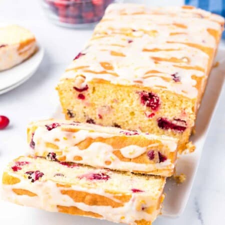 Sliced cranberry orange bread topped with glaze at an angle on a platter to see the entire sliced loaf.