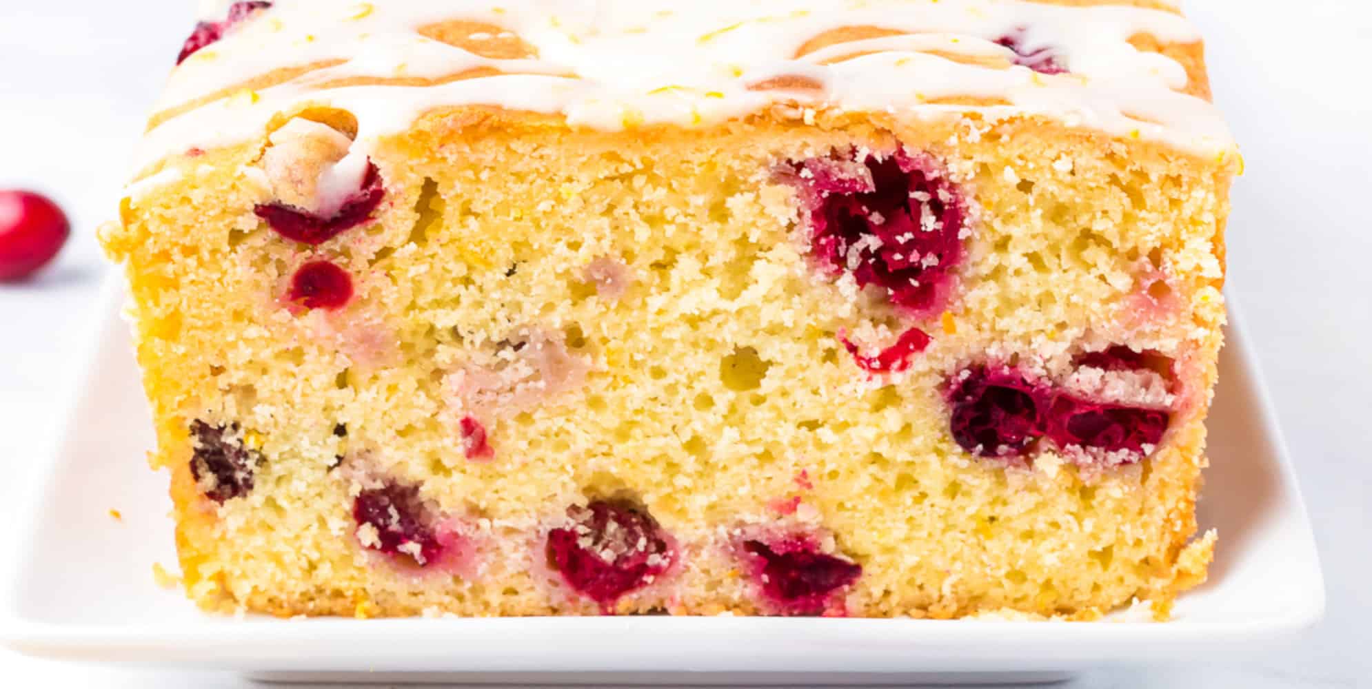 A wide view of the end of a loaf of sliced cranberry orange bread with glaze on top on a platter.