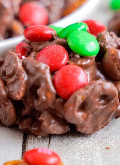 Close up of a chocolate cluster full of pretzels topped with green and red M&Ms on a counter from the side.