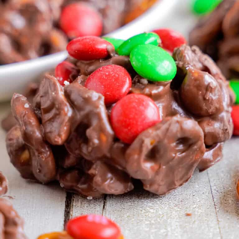 Close up of a chocolate cluster full of pretzels topped with green and red M&Ms on a counter from the side.