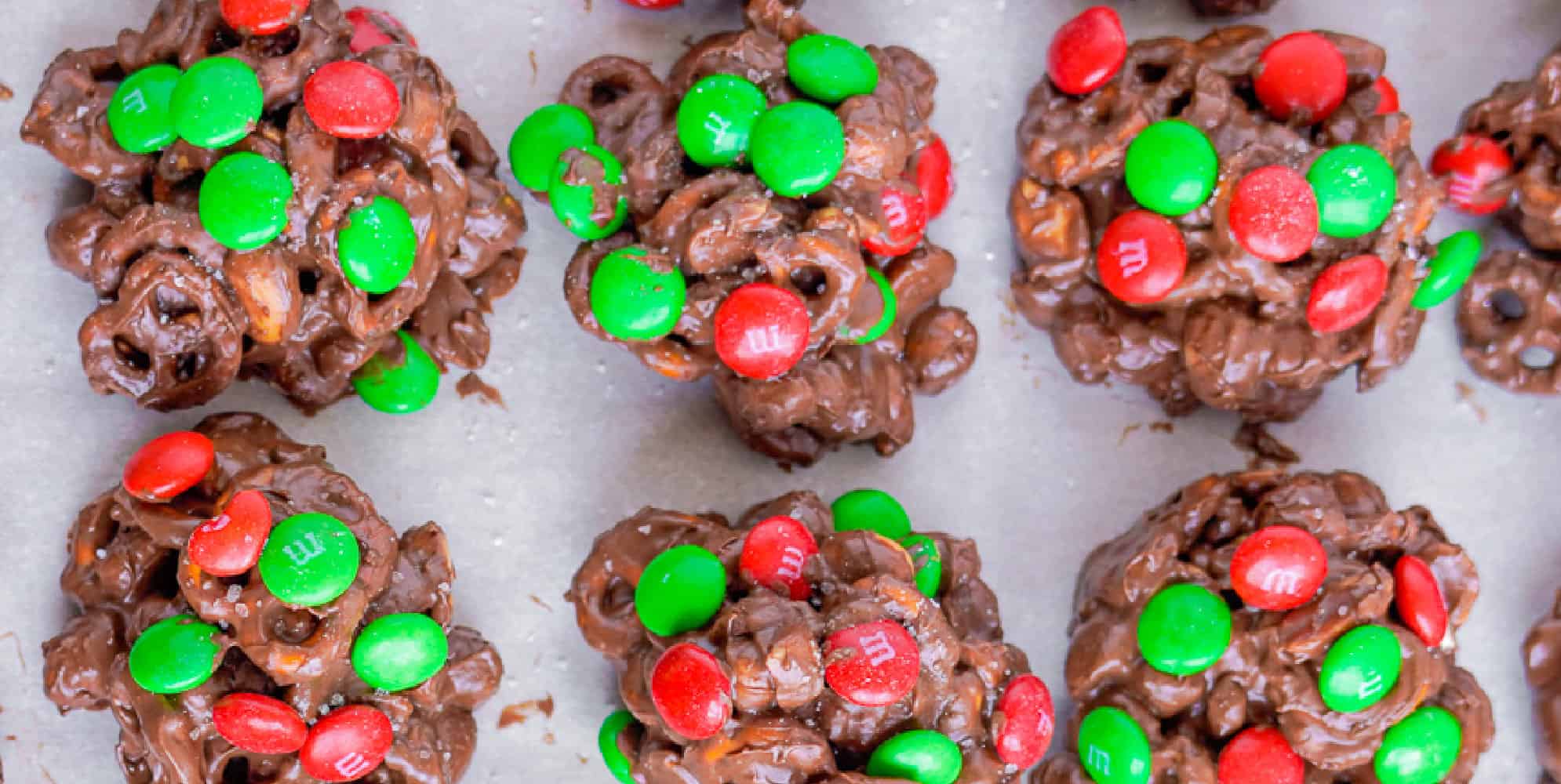 Wide view of chocolate crockpot candy lined up on parchment paper with red and green M&Ms on top.