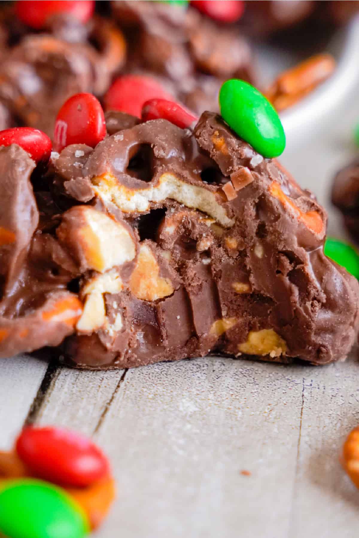 Chocolate crockpot candy missing a bite close up to see the pretzels inside with red and green M&Ms on top.