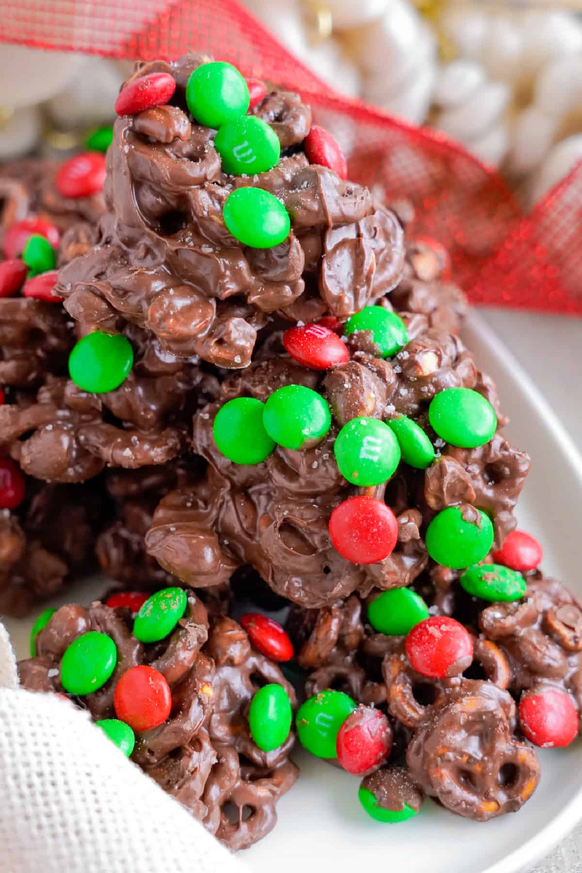 Chocolate cluster crockpot candy piled on a platter covered in red and green M&Ms from the side.