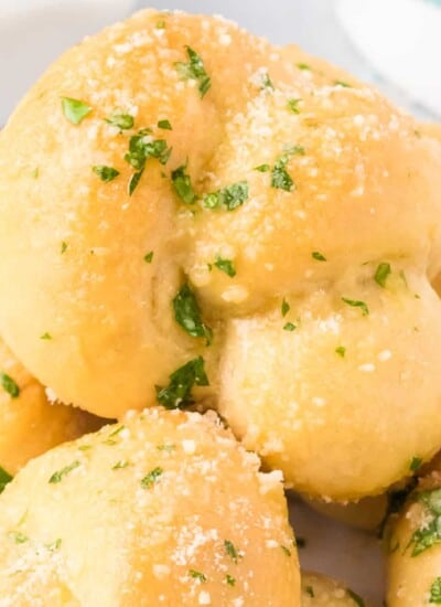 Close up on a garlic knot covered in garlic, cheese and parsley from the side.