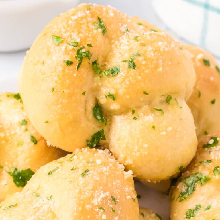 Close up on a garlic knot covered in garlic, cheese and parsley from the side.