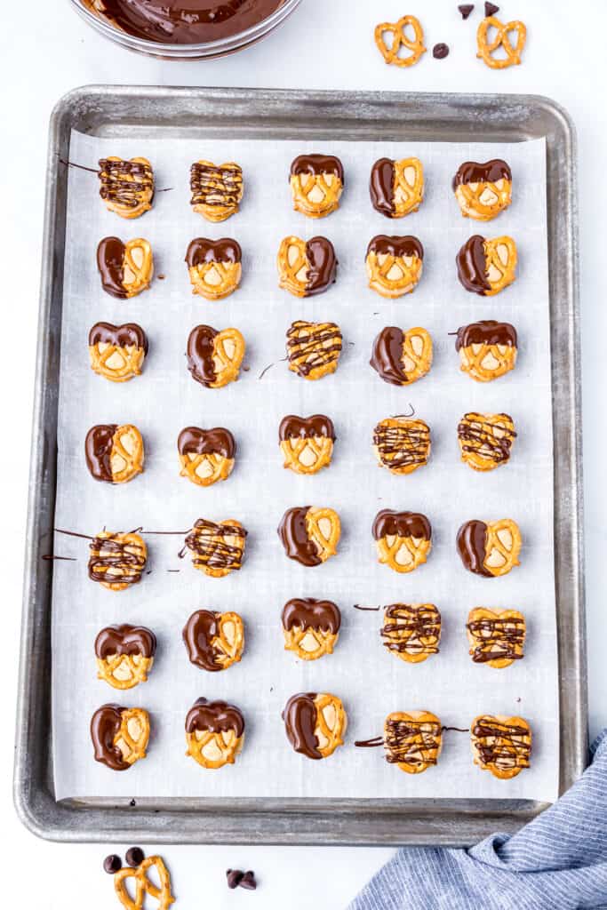 A tray of buckeye peanut butter pretzels with half of them dipped in chocolate halfway and half drizzled with chocolate.