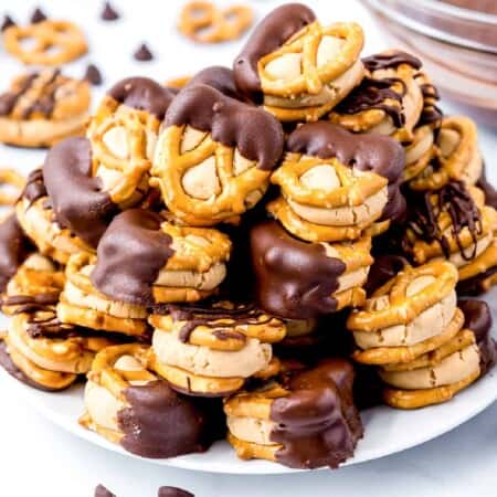 Peanut butter stuck between small pretzels dipped in chocolate stacked high on a plate from the side on a counter.