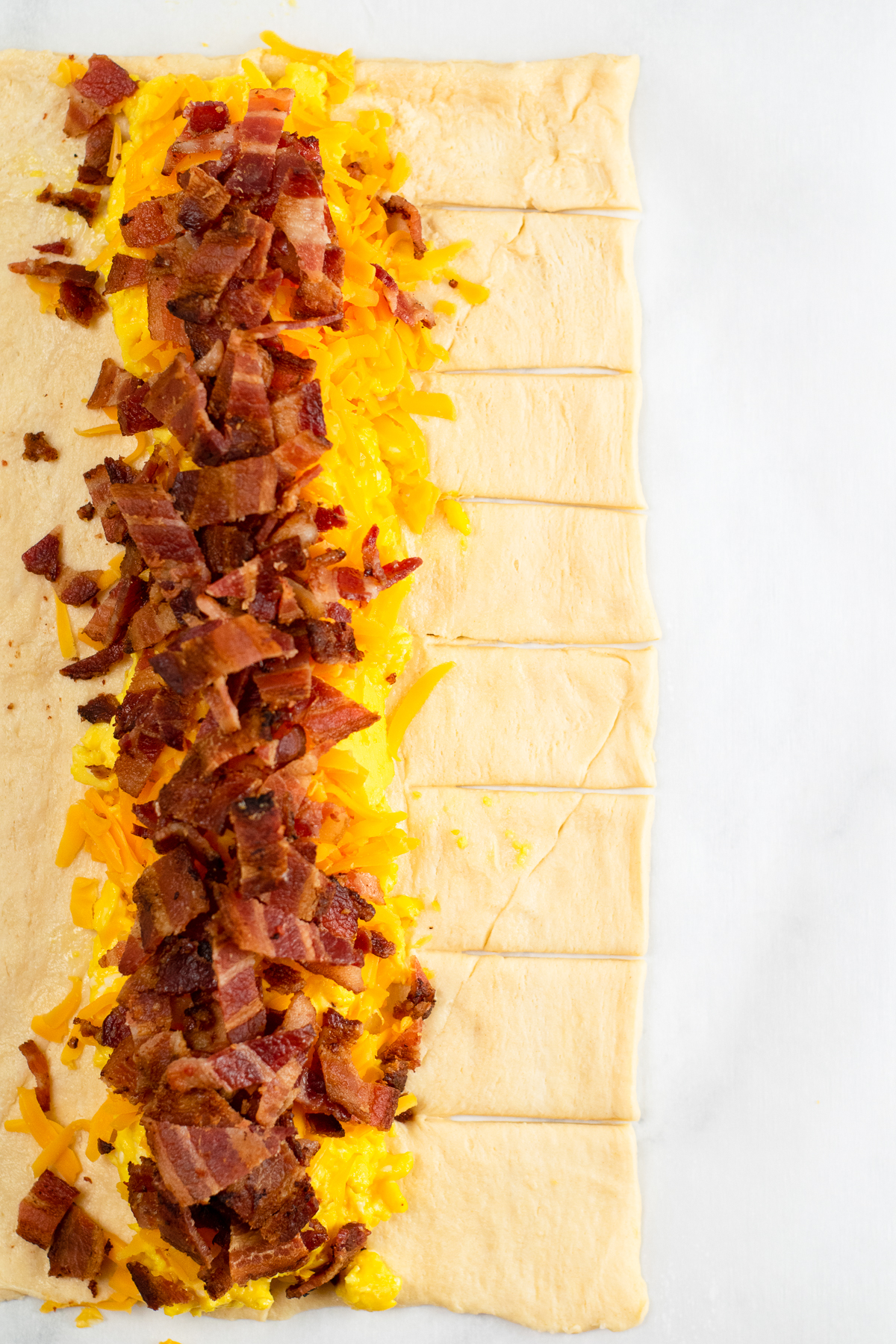 Close up of cut dough strips on one side of the braid with bacon, cheese and eggs in the middle of the dough.