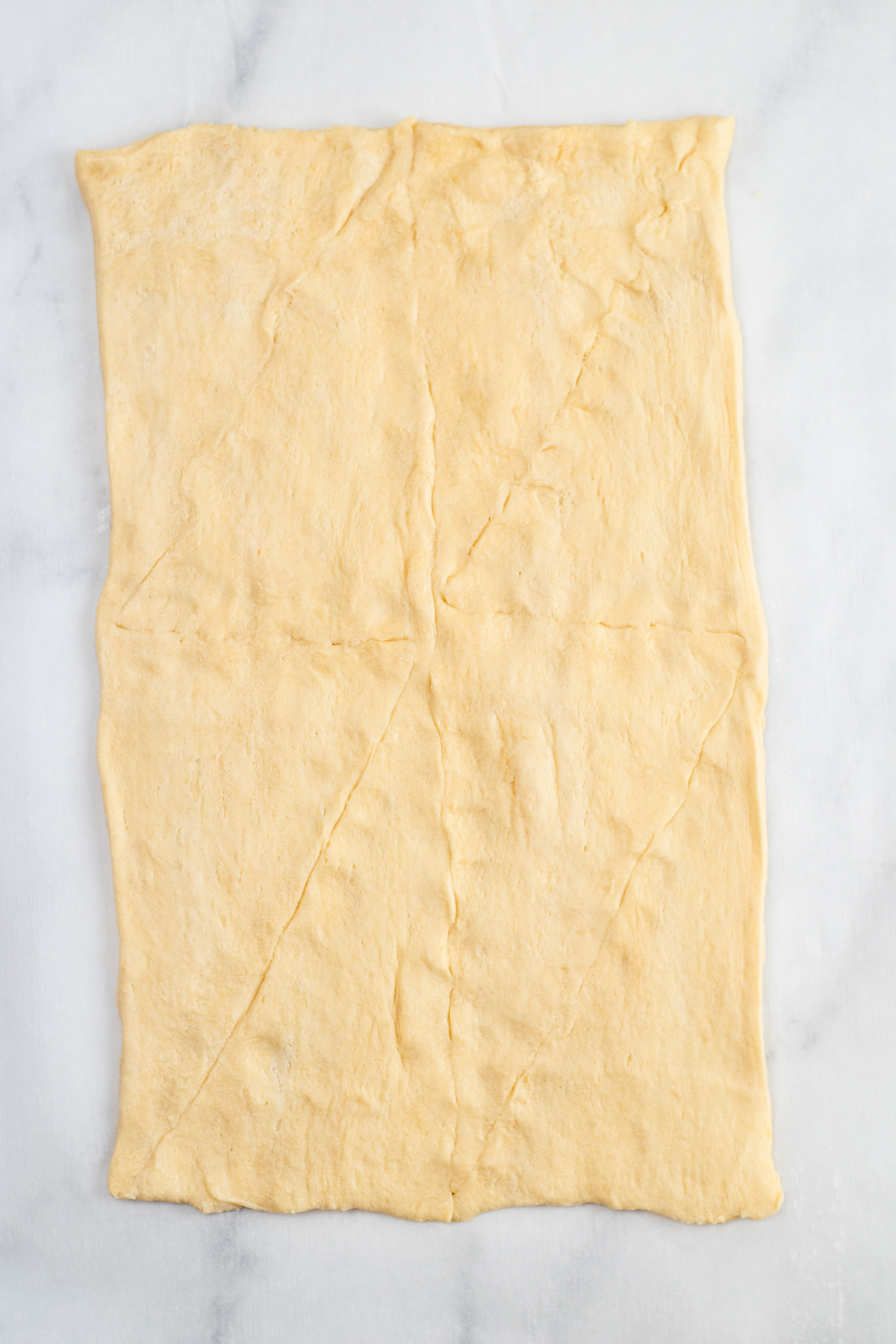 Crescent roll dough rolled out into a sheet with the seams pressed closed on a counter from above.