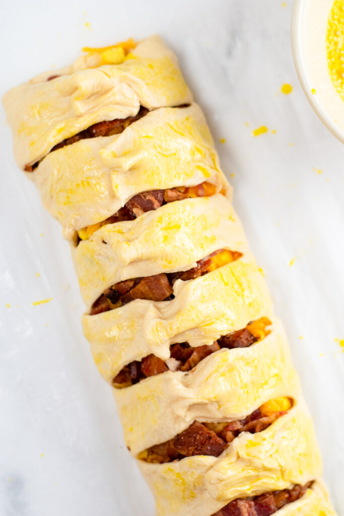 Breakfast Crescent roll braid being covered in egg wash.