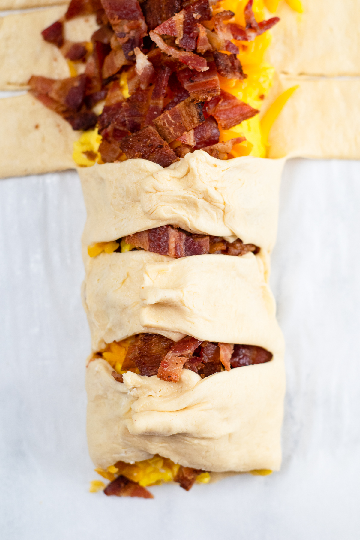 Folding crescent dough strips over the bacon, eggs and cheese.