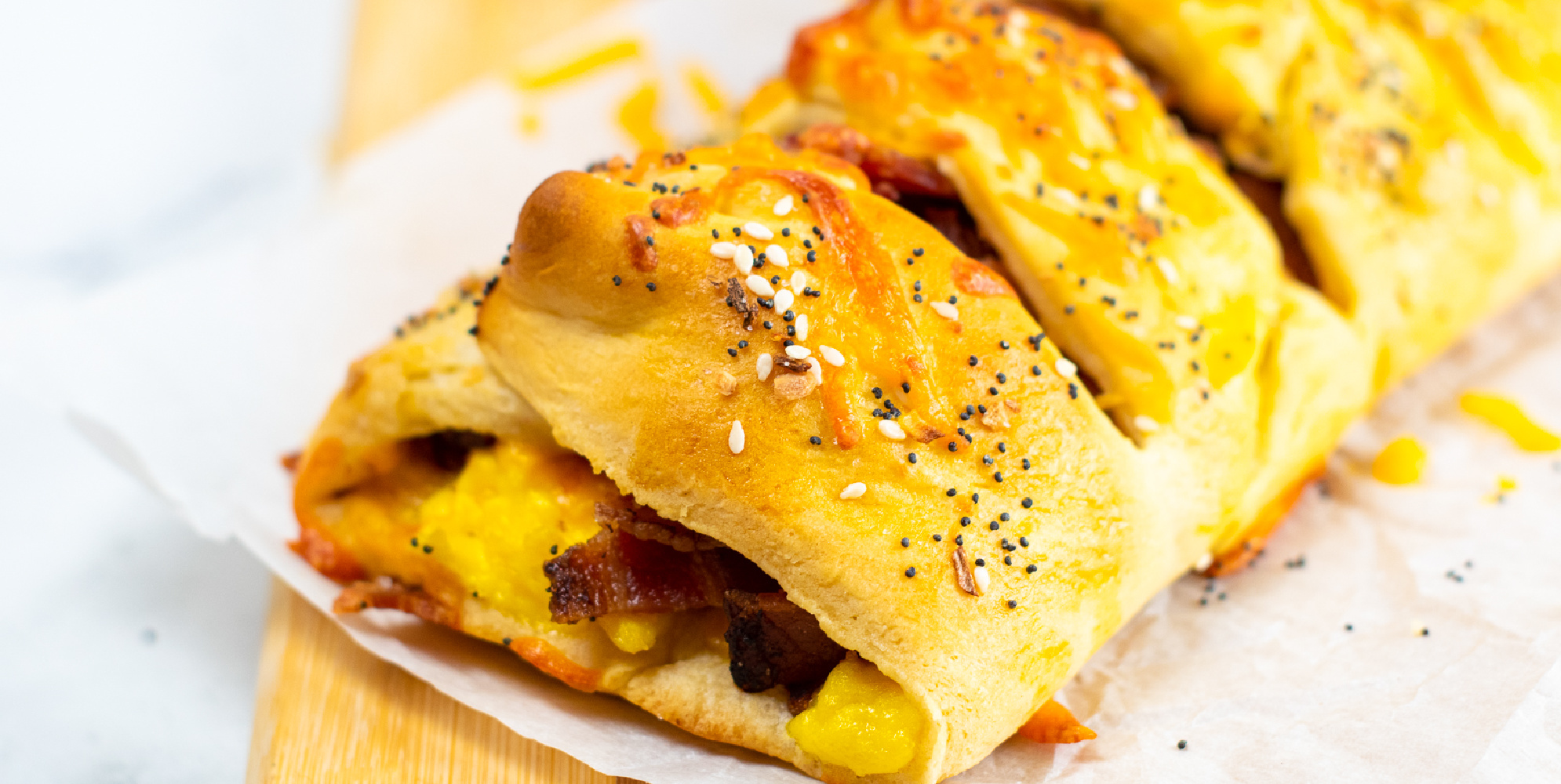 Wide view of the end of a breakfast braided dough stuffed with bacon egg and cheese on a cutting board up close.