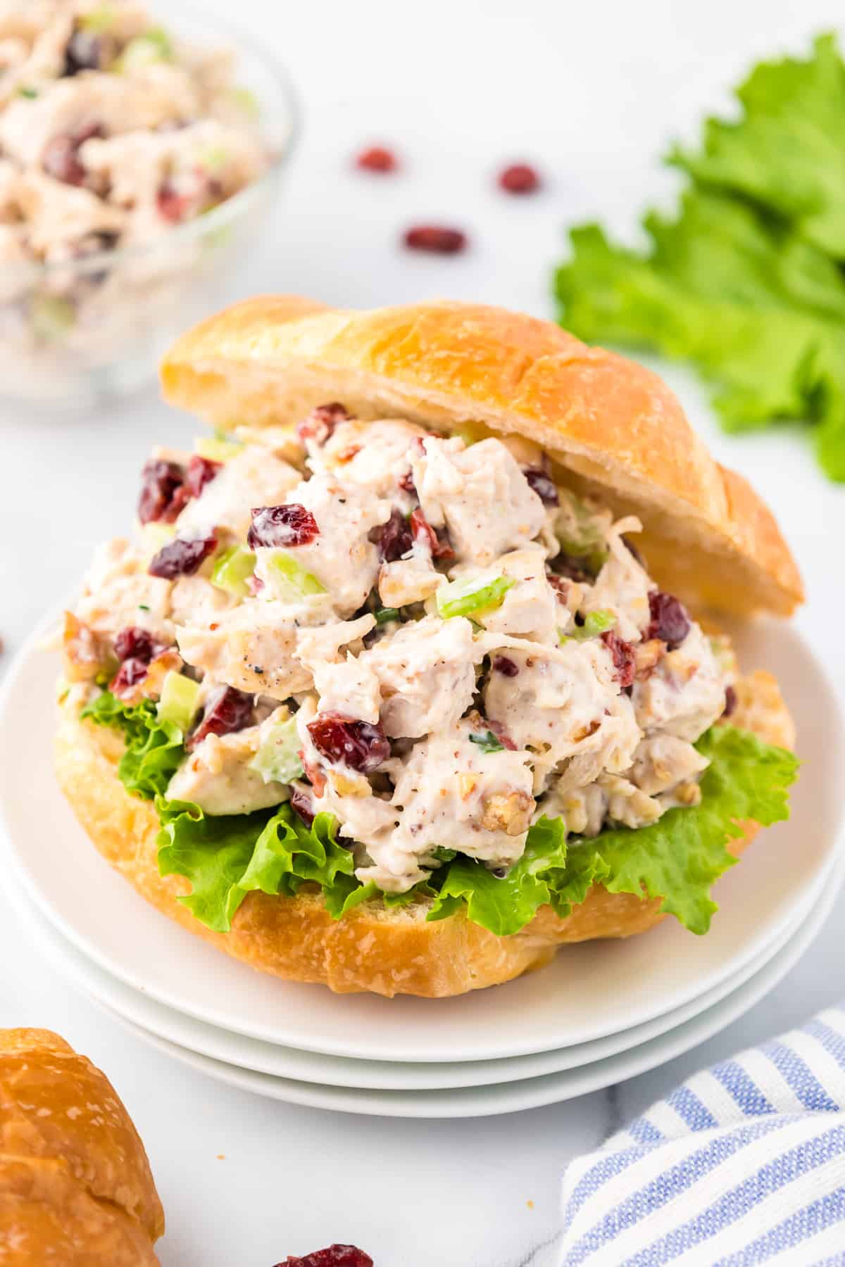 Cranberry Pecan Chicken Salad piled high on a croissant with lettuce to make a sandwich on a plate.