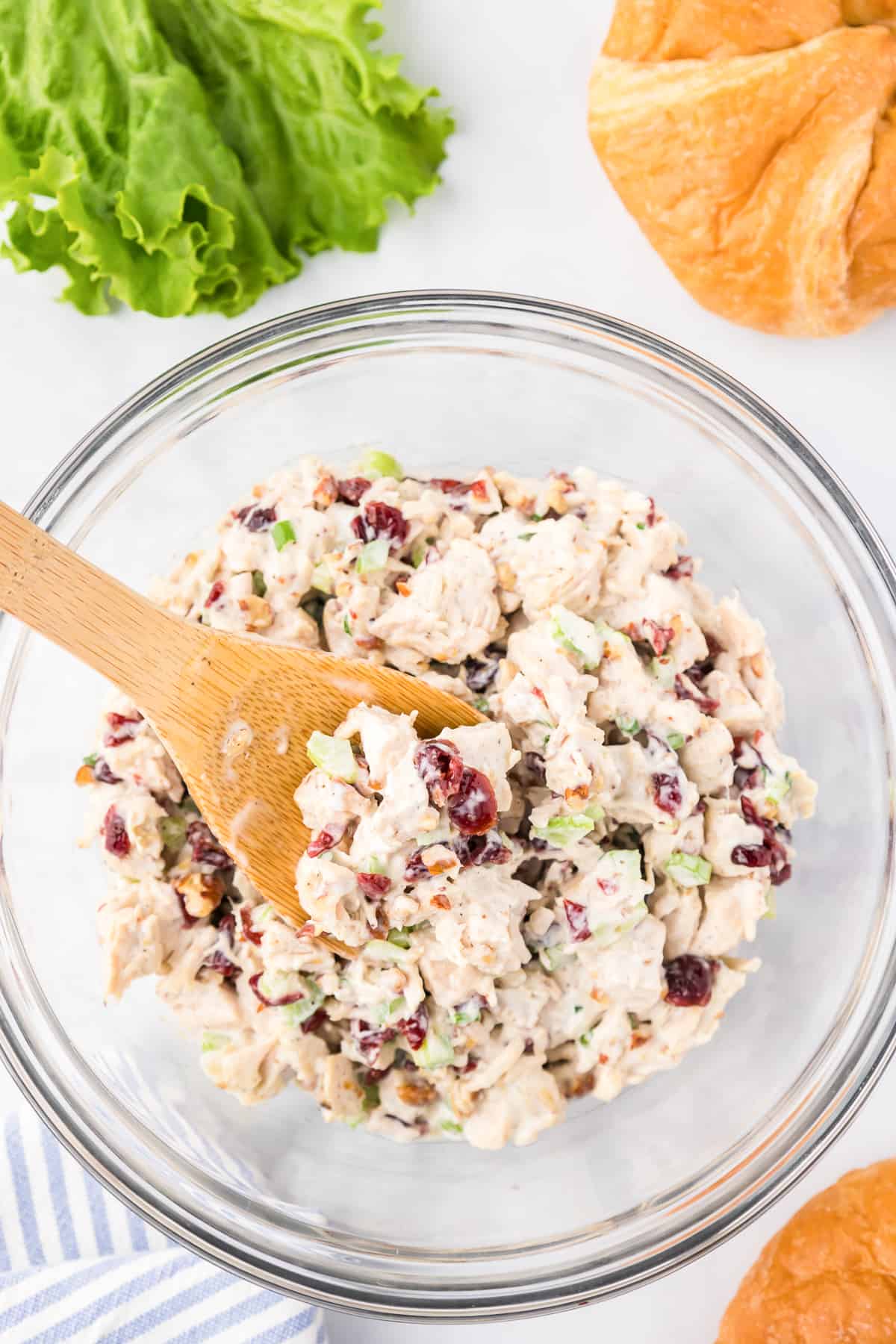 Cranberry pecan chicken salad being mixed with dressing in a large bowl from overhead on a counter with a wooden spoon.