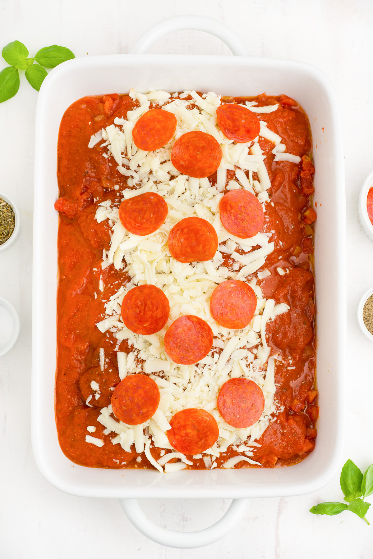 Raw chicken covered in tomato sauce, diced tomatoes, pepperoni and cheese in a baking dish from overhead.
