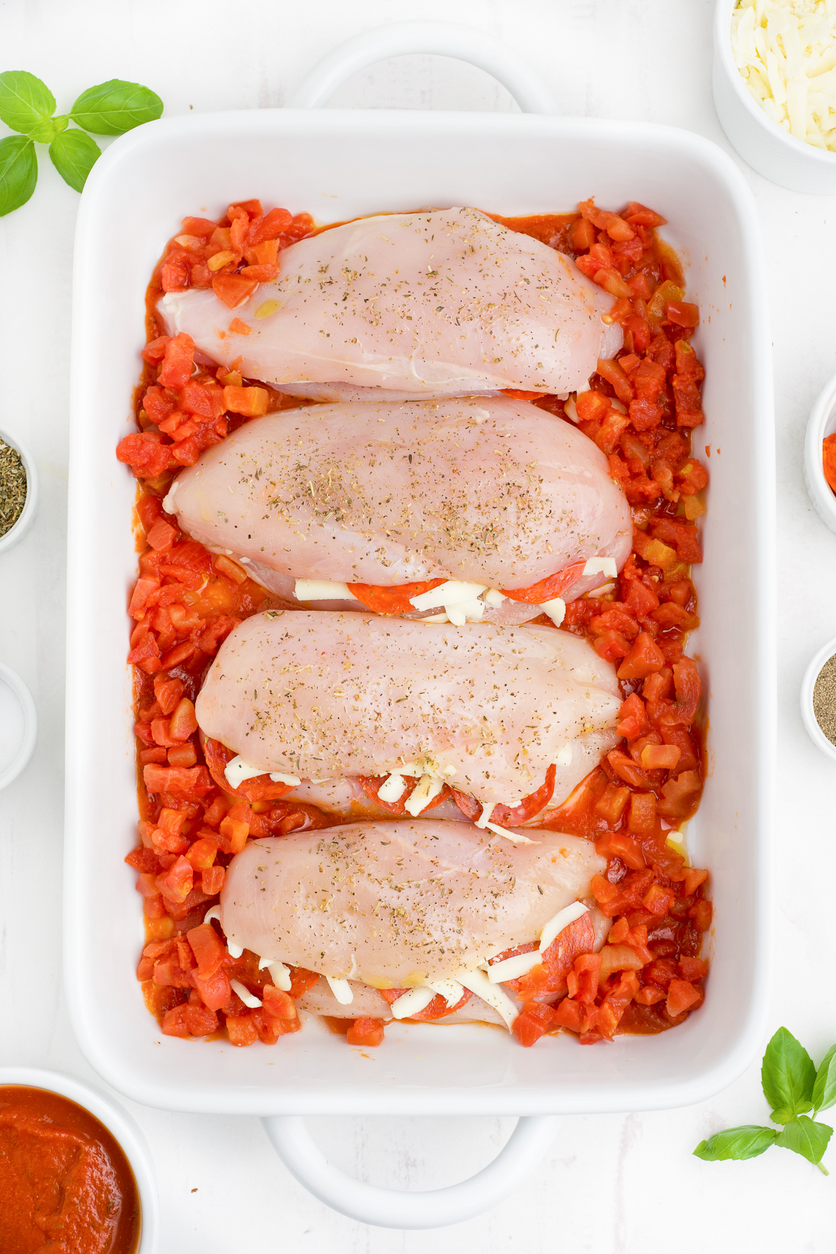 Chicken breasts stuffed with cheese and pepperoni surrounded by diced tomatoes in a baking dish from overhead.