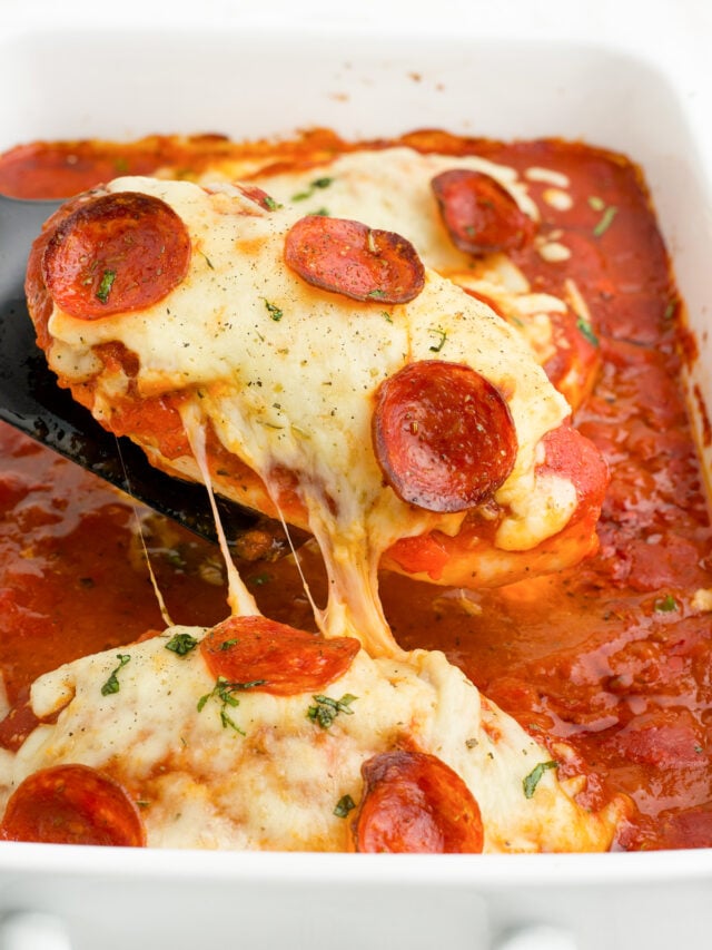 Chicken covered in cheese and pepperoni being lifted from the pan with a spatula with melty cheese pulling.