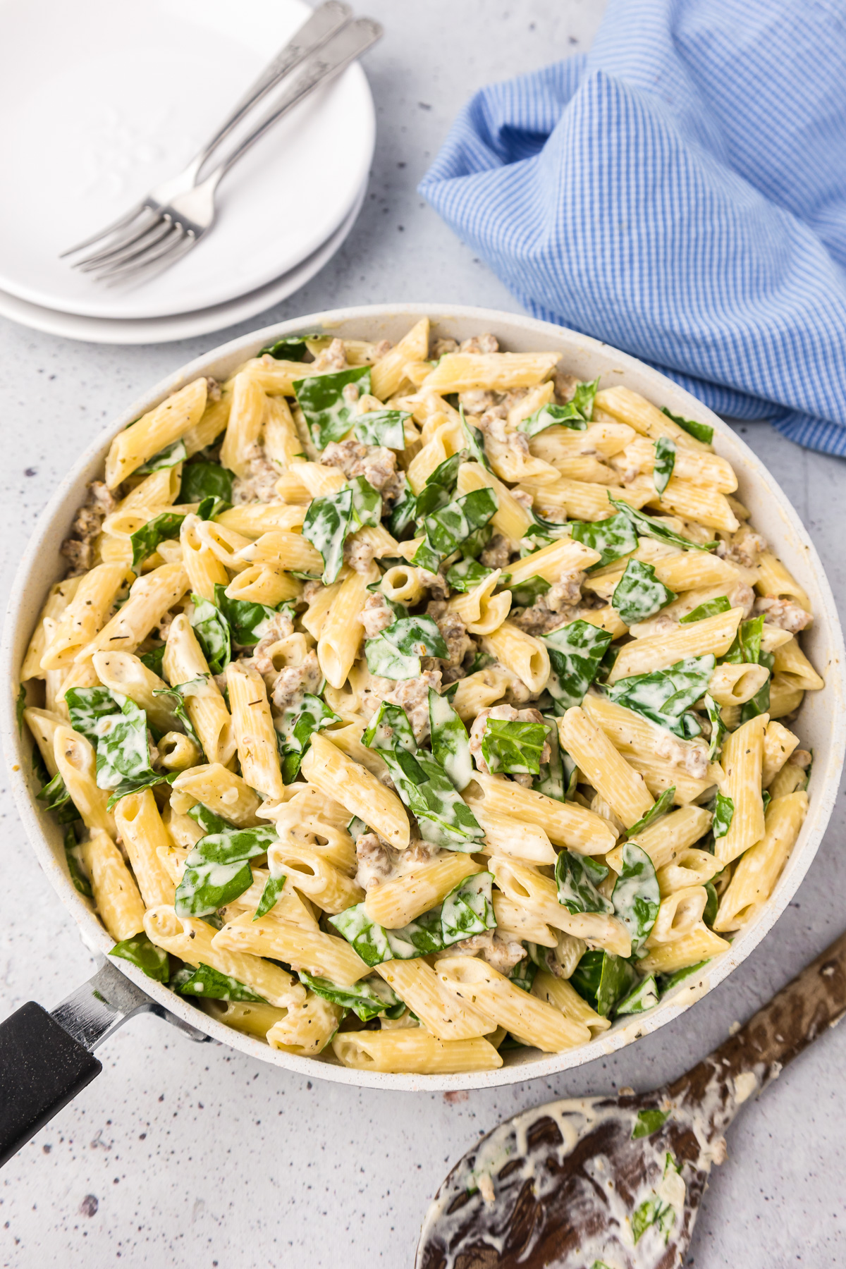 Creamy sausage pasta with a white sauce and spinach in a skillet from above on a counter.